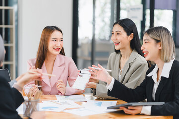 Group of professional businesswomen discussing documents and using a calculator during a collaborative office meeting.
