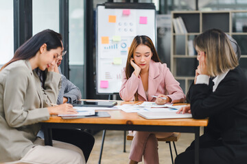 Business team looking stressed and overwhelmed during a meeting, with documents and charts spread on the table.
