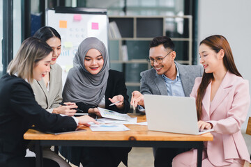 Diverse business team analyzing data and discussing strategies during an office meeting, using documents and a laptop.