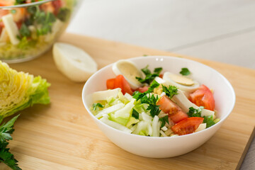 fresh vegetable salad, cabbage, tomatoes in a bowl on a wooden table