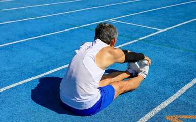 Senior Asian athlete doing stretching warm up for running in the professional blue track for...