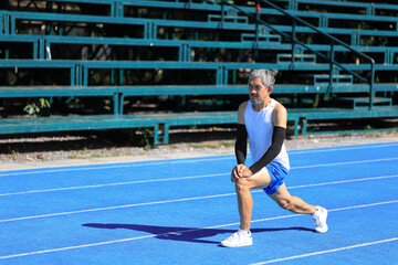 Senior Asian athlete doing stretching warm up for running in the professional blue track for professional exercise, sport training workout and healthy for longevity concept