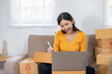 Smiling woman preparing a package for shipping while sitting on a sofa surrounded by boxes. Small...