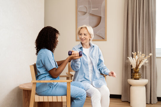 Elderly Woman In Physical Therapy Session With Female Therapist. Providing Care Through Exercise And Encouragement