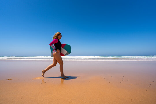 Beautiful woman holding bodyboard  running on sunny beach Bordeira praia, Algarve , Portugal