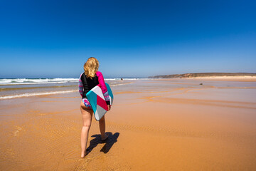 Beautiful woman holding bodyboard  walking on sunny beach Bordeira praia, Algarve , Portugal