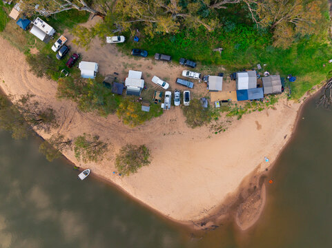 Aerial view of a row of caravans and tents on a sandy beach alongside a murky river