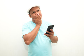 Adult Asian man thinking about something while holding mobile phone
