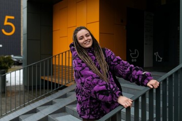 Stylish young woman with dreadlocks stands against the background of an orange house