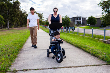 Interracial couple on walk down footpath with kid in push trike pram