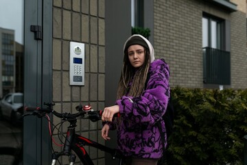 Stylish informal woman with dreadlocks wearing a purple jacket rides a bicycle