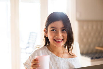 Close-up photo of a young girl smiling while holding a white cup
