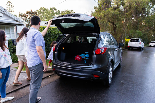 Family of four standing on the street near car parked in front of house with boot open