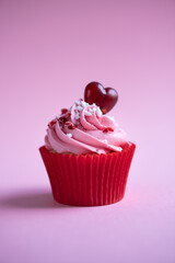 Delicious strawberry cupcake on pink background with heart candy and red sprinkles