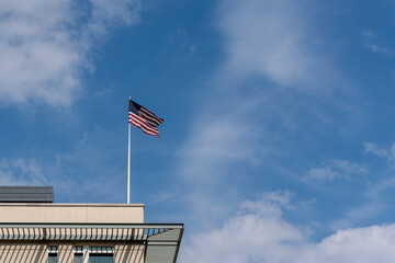 Fototapeta premium A flag is flying on a pole in front of a building. The sky is blue with some clouds