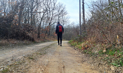 A man dressed in black with a red backpack walks along a rural road