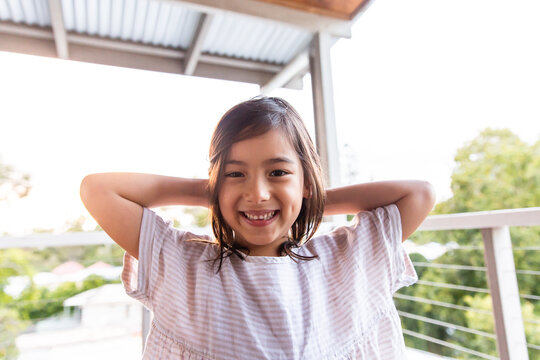 A young girl smiling at the camera with her hands at the back of her head