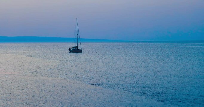 Barca a vela alla fonda in mare calmo con promontorio del Gargano (Puglia) sullo sfondo con cielo nuvoloso