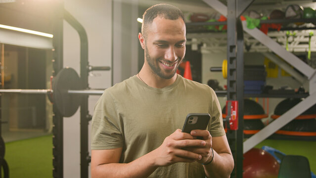Smiling happy African American man sportsman athlete guy fitness trainer gym instructor male smile browsing mobile phone social media looking at camera scrolling smartphone app sport betting chatting - Powered by Adobe