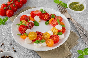Caprese salad with cherry tomatoes, mini mozzarella, pesto sauce and fresh basil in a white plate. Healthy vegetarian meal.