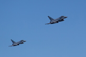 Two Typhoon Eurofighter jets flying over town centre with missiles on way to mission. Modern airforce fighter jets in formation with dramatic amazing sky and clouds