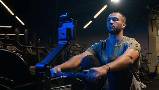 Sport functional training exercise biceps back muscles healthy African American trainer strong man sporty male guy athlete sportsman bodybuilder in gym pulling rope workout pull rowing machine sitting