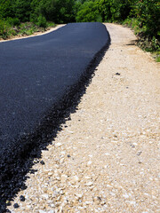 Newly paved rural road in lush green forest with contrasting asphalt and gravel