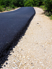 Freshly paved road with greenery, contrasting new asphalt and gravel