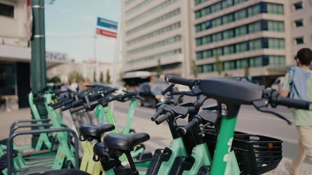 Multiple green electric scooters parked on a city street, offering urban transportation options near modern office buildings. A sustainable choice for commuting in a bustling urban environment.