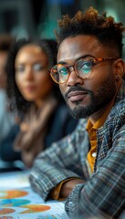 Business professionals in a meeting, focusing on a confident man with glasses. Collaborative work environment with charts and graphs.
