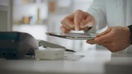 Pharmacist assistant uses skills working on an electronic tablet in the pharmacy department. A working Caucasian man holds touch tablet in his hands checking the expiration date of medicines, medicine