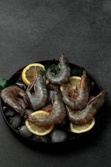 Large King prawns on lemon slices and ice. Black plate. Black background