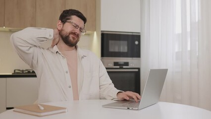 Young man in casual wear suffering from neck pain in home office after long time sitting in incorrect posture by laptop.