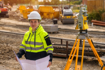 Mature Female Construction Worker Holding Plans Near Survey Equipment