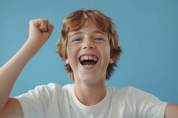 A happy young boy in a white t-shirt stands confidently against a vivid blue backdrop. His bright smile and natural charm shine in the well-lit image, capturing the joy of childhood
