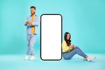 Cool mobile app. Couple sitting near huge smartphone with mockup blank screen, using gadgets and promoting your product or service