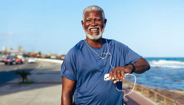 Mature African American man exercising seaside with fitness watch and music - Powered by Adobe