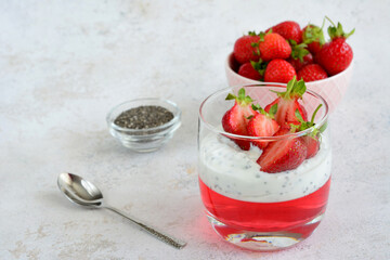 a glass of strawberry dessert next to a spoon and a bowl of chia seeds 