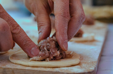 Chef's hands fingers close-up making pelmeni from dough and meat. Preparing dumplings. Traditional food
