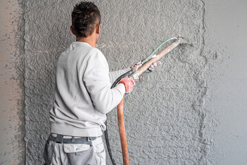 Machine plastering. Applying gypsum plaster by mechanized method on a wall. A worker hand removes excess plaster with leveler.