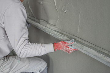 Machine plastering. Applying gypsum plaster by mechanized method on a wall. A worker hand removes...