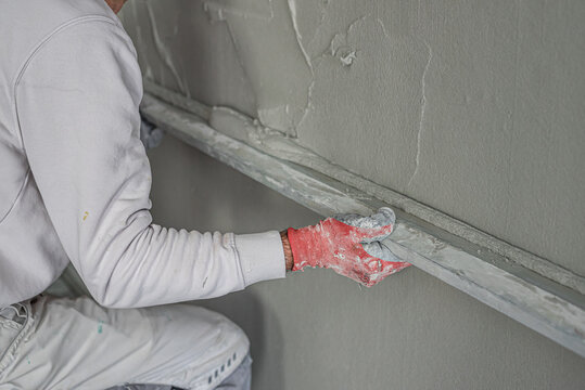 Machine plastering. Applying gypsum plaster by mechanized method on a wall. A worker hand removes excess plaster with leveler.