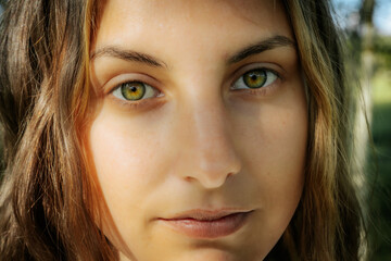 Fototapeta premium Intimate close-up of a womans face highlighting her striking green eyes and natural complexion, with a serene expression and natural background.