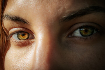 Fototapeta premium Intimate close-up of a womans face highlighting her striking green eyes and natural complexion, with a serene expression and natural background.