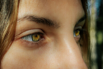 Fototapeta premium Intimate close-up of a womans face highlighting her striking green eyes and natural complexion, with a serene expression and natural background.