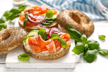 Salmon sandwiches with bagel, salted fish, fresh cucmber, onion and basil on white background. Healthy breakfast with salmon toasts