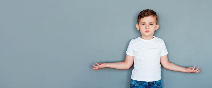 Confused little kid boy wearing basic white t-shirt spreading hands looking camera isolated on gray color background children studio portrait. Childhood lifestyle concept