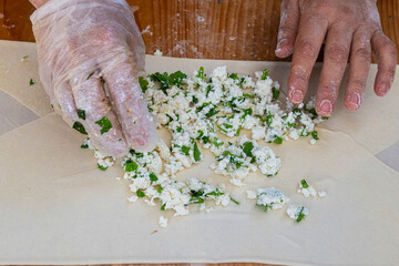A woman puts a mixture of cheese and parsley in a traditional Turkish pancake.