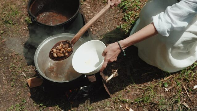 Woman with a spoon mixes empty shells from garden snails in a saucepan, which are cooked for cleaning in boiling water. The process of cooking a gourmet dish. French cuisine. Close-up. 
