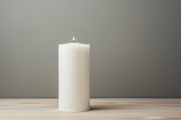 Single lit white candle presents a calming ambiance on a wooden surface with a soft gray backdrop